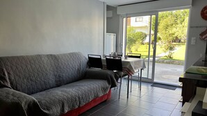 Una sala de estar moderna con un sofá gris, una mesa de comedor con sillas y un ventanal corredero que da a un jardín.