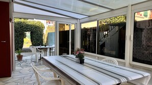 Un porche cubierto con una mesa y sillas, una planta en maceta y vistas al jardín.