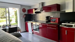 Una cocina compacta con armarios rojos, un microondas, una cafetera y un televisor sobre un mueble.