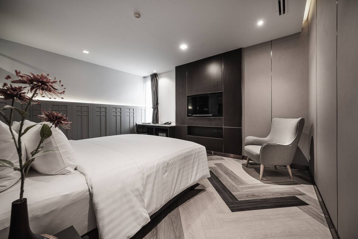 Une chambre moderne avec un grand lit, un téléviseur fixé au mur et un fauteuil.