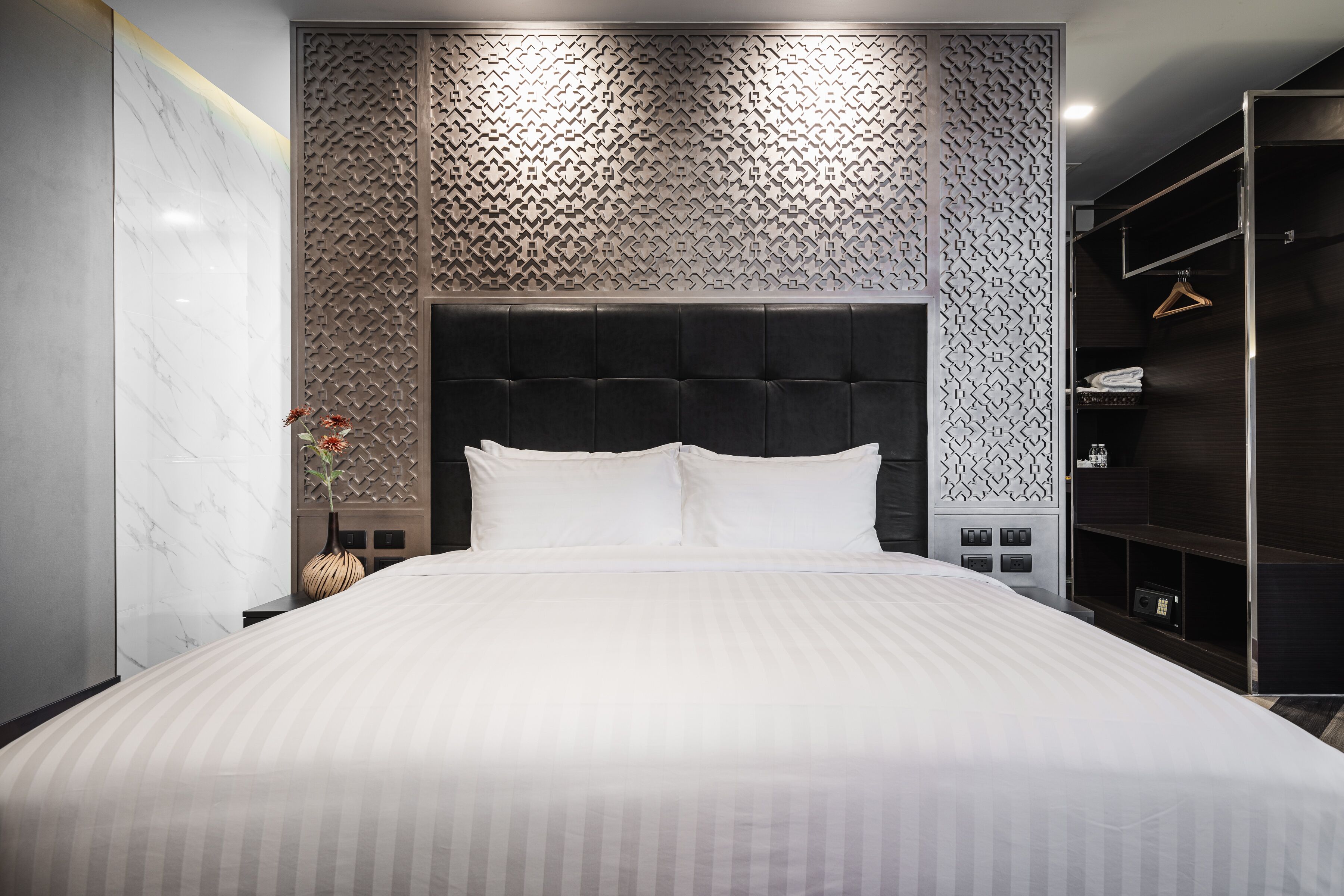 Habitación de hotel moderna con una cama grande, un cabecero oscuro, un papel tapiz estampado y un armario.