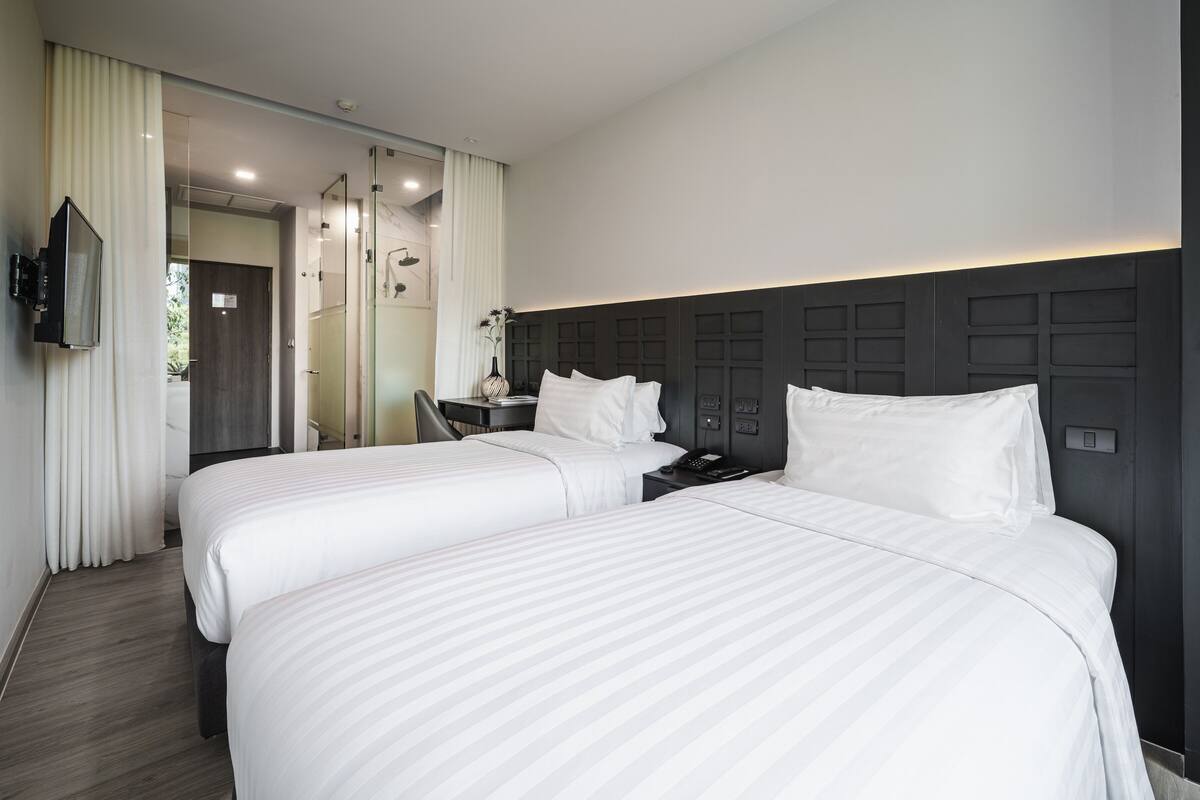 Une chambre d’hôtel avec deux lits, une télévision, un bureau et une salle de bain visible à travers une porte en verre.