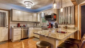 Una cocina moderna con armarios blancos, electrodomésticos de acero inoxidable, encimeras de granito y una isla central con taburetes de bar.