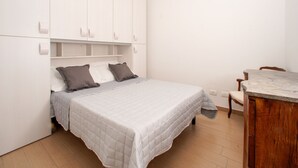A bedroom with a bed, a wooden desk, and a wardrobe.