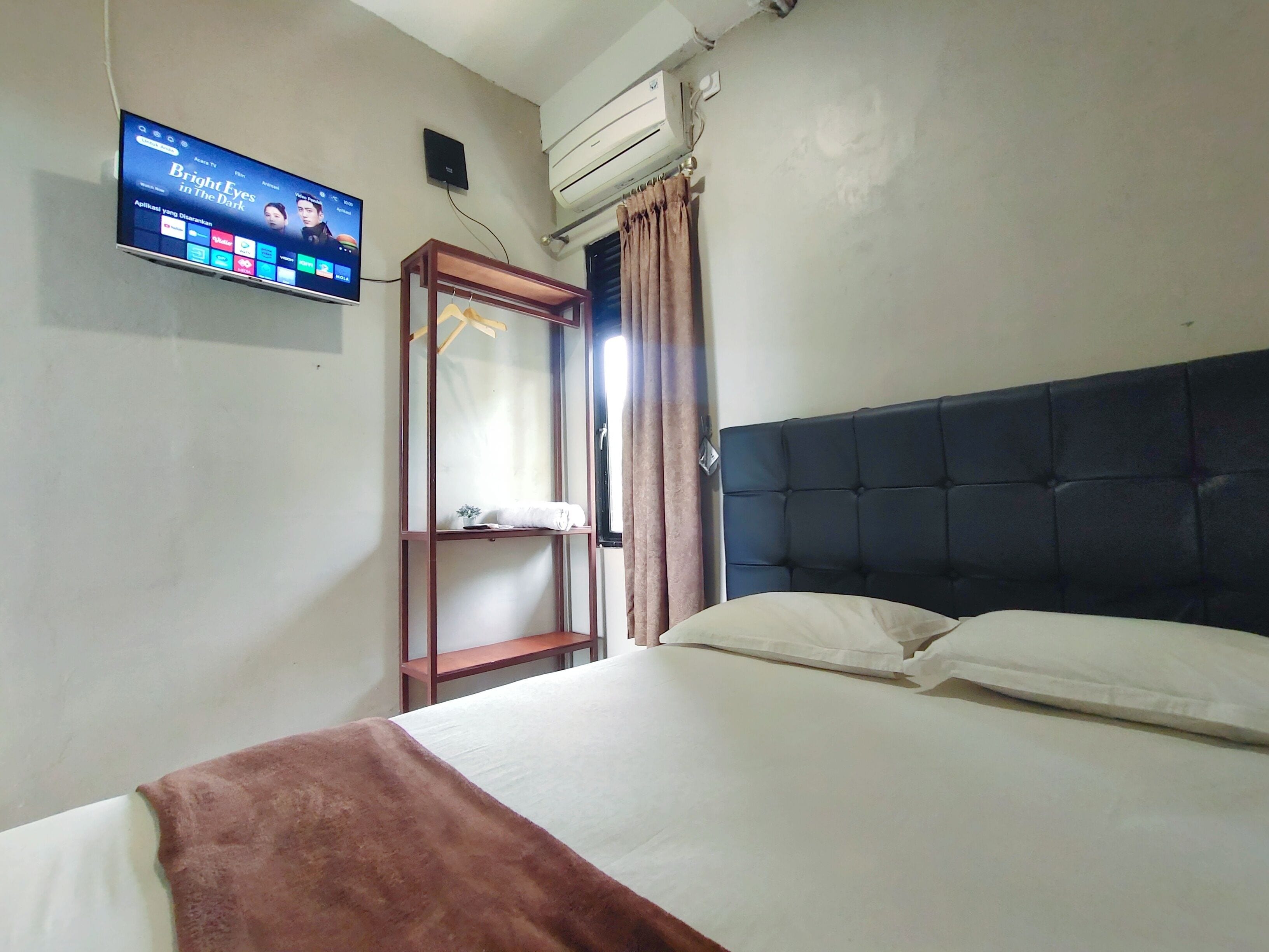 Habitación de hotel con cama, televisor montado en la pared, aire acondicionado y armario con espejo.