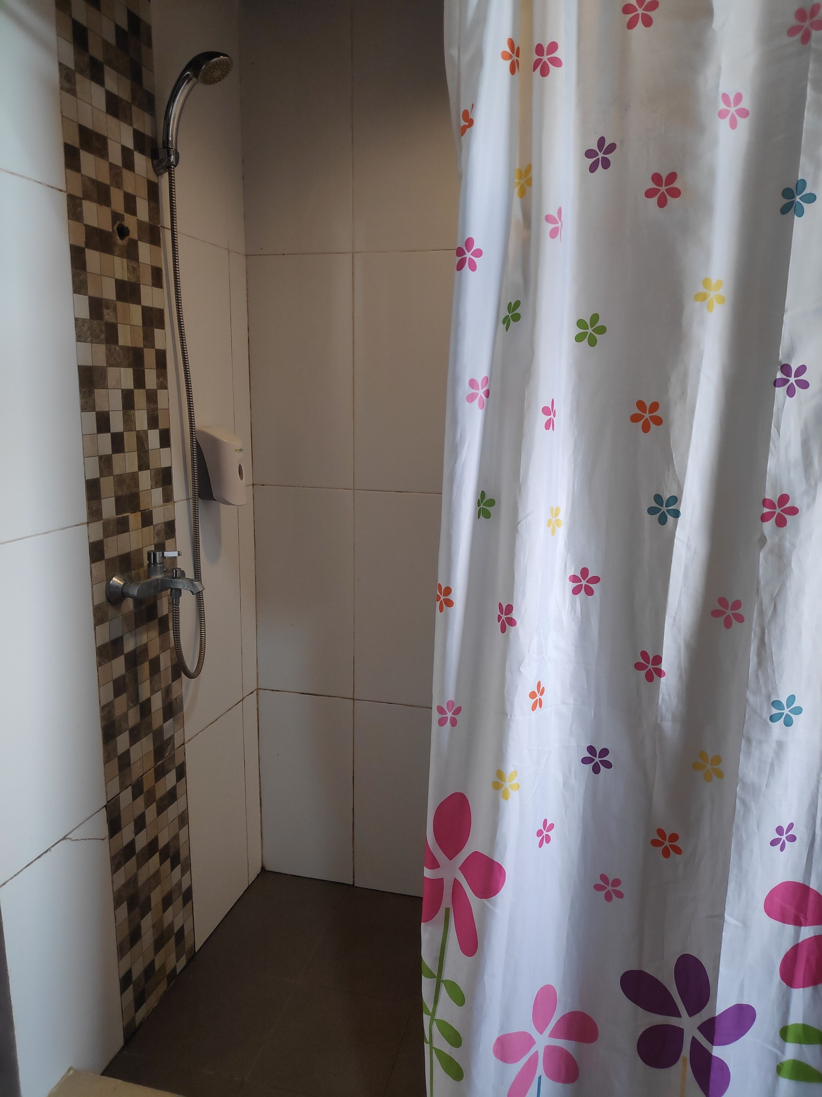 Een badkamer met een douche, betegelde muren en een douchegordijn met bloemenprint.