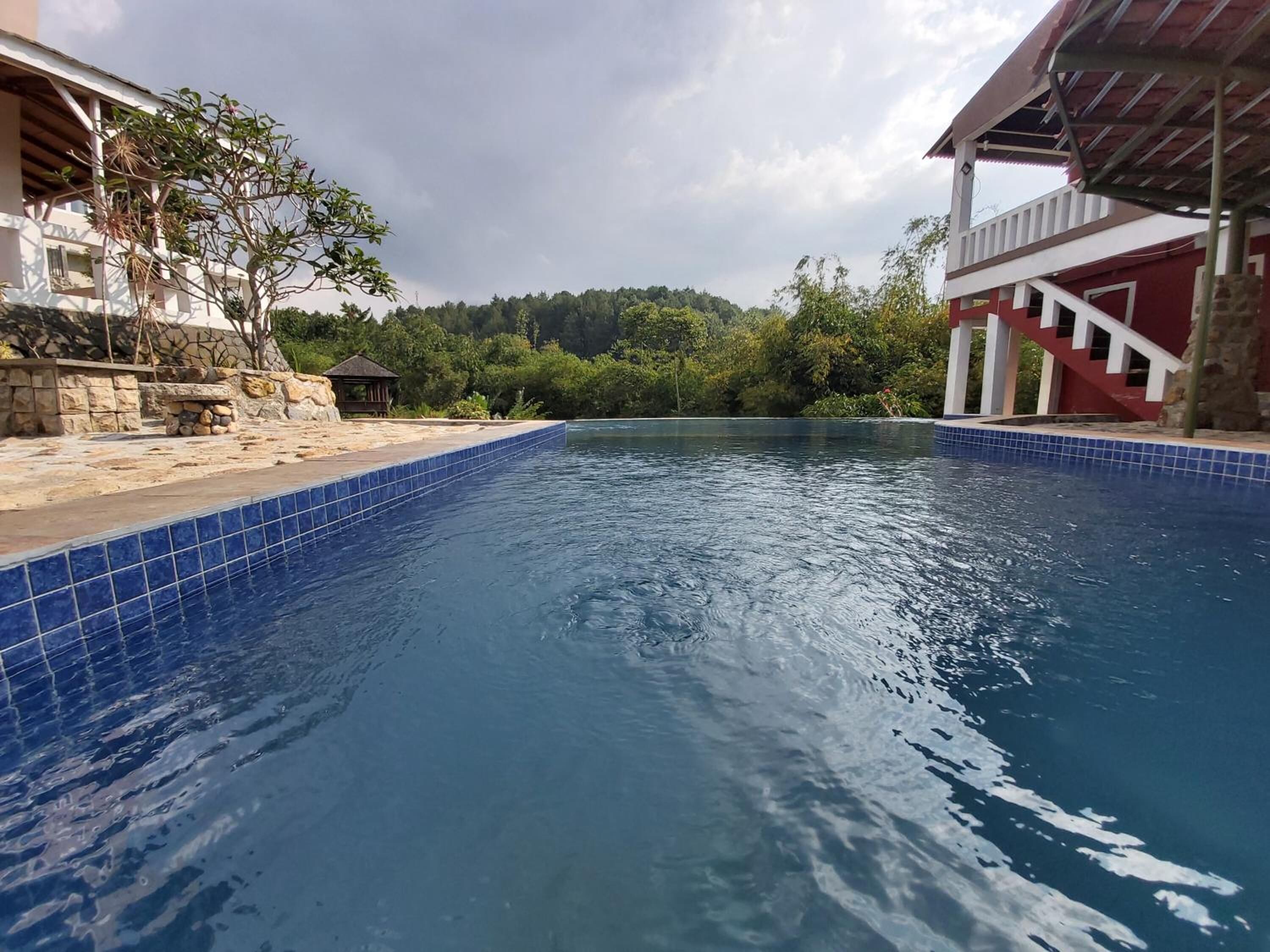 Una piscina con azulejos azules, rodeada de estructuras de piedra y un edificio rojo con una escalera.