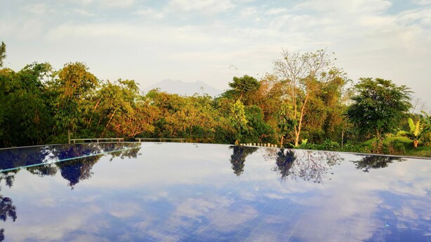 Una piscina infinita con reflejo del cielo y árboles circundantes.