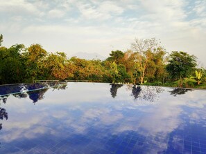 Una piscina infinita con reflejo del cielo y árboles circundantes.