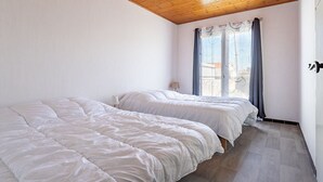 Une chambre avec deux lits, un plafond en bois, une fenêtre avec des rideaux et une table de chevet.