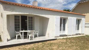 Un bâtiment blanc avec un toit en tuiles, une terrasse avec une table et des chaises, et une pelouse.
