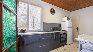 Une cuisine moderne avec des meubles noirs, un plan de travail blanc, un four à micro-ondes, un réfrigérateur et une fenêtre avec des stores à motifs.