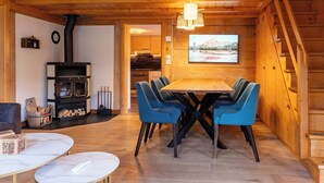 A cozy wooden interior with a dining table surrounded by chairs, a fireplace, and a large window with a scenic view.