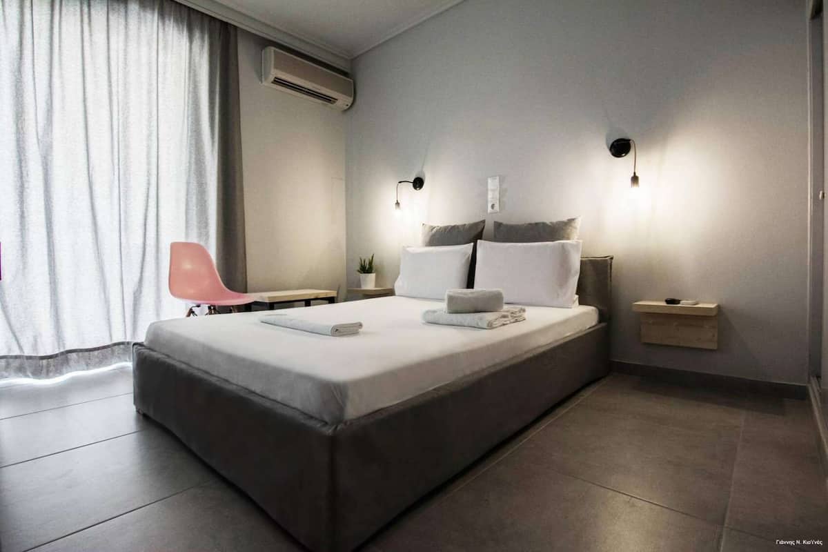A modern hotel room with a large bed, a bedside table, a chair, and a small bedside table with a lamp.