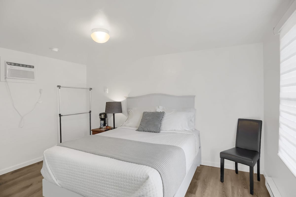 A neatly arranged bedroom with a bed, a chair, a nightstand, and a lamp.