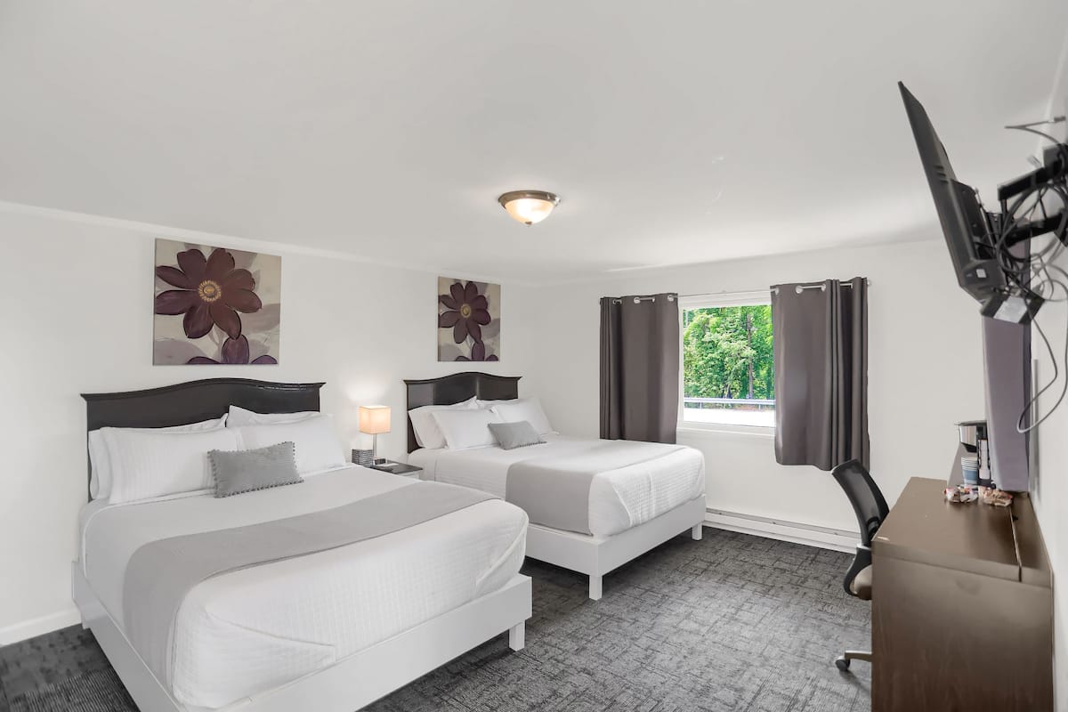 A hotel room with two beds, a desk, a chair, and a TV.