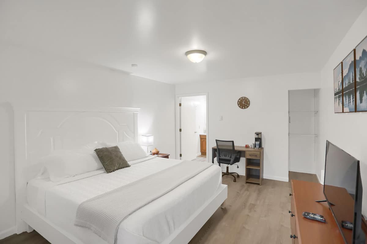 A hotel room with a large bed, a desk with a computer, a TV, and a clock on the wall.