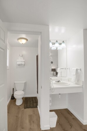 A bathroom with a toilet, sink, and mirror. There is a towel rack above the sink and a light fixture above the toilet.