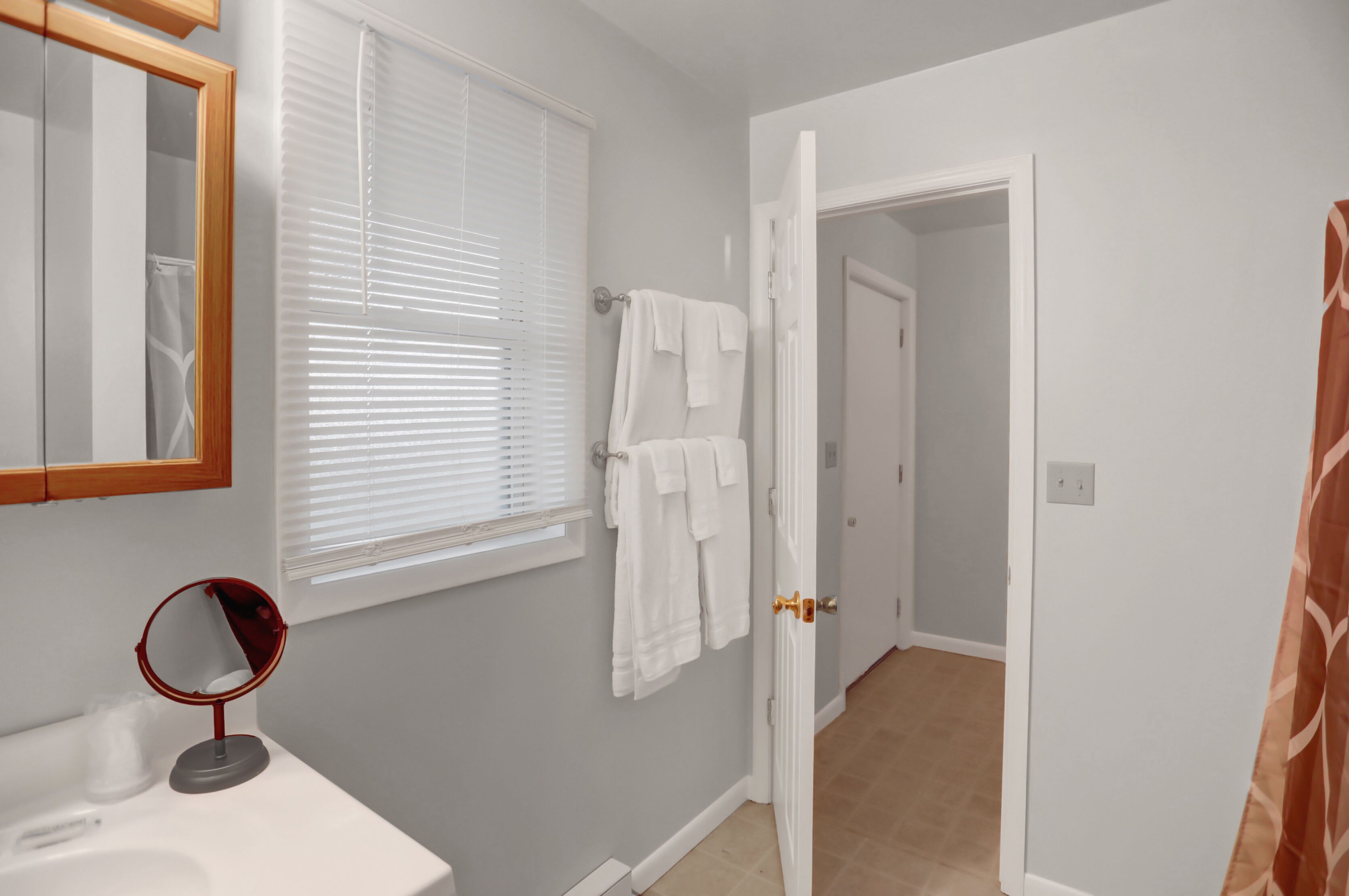 A bathroom with a sink, mirror, towel rack, and a door leading to another room.
