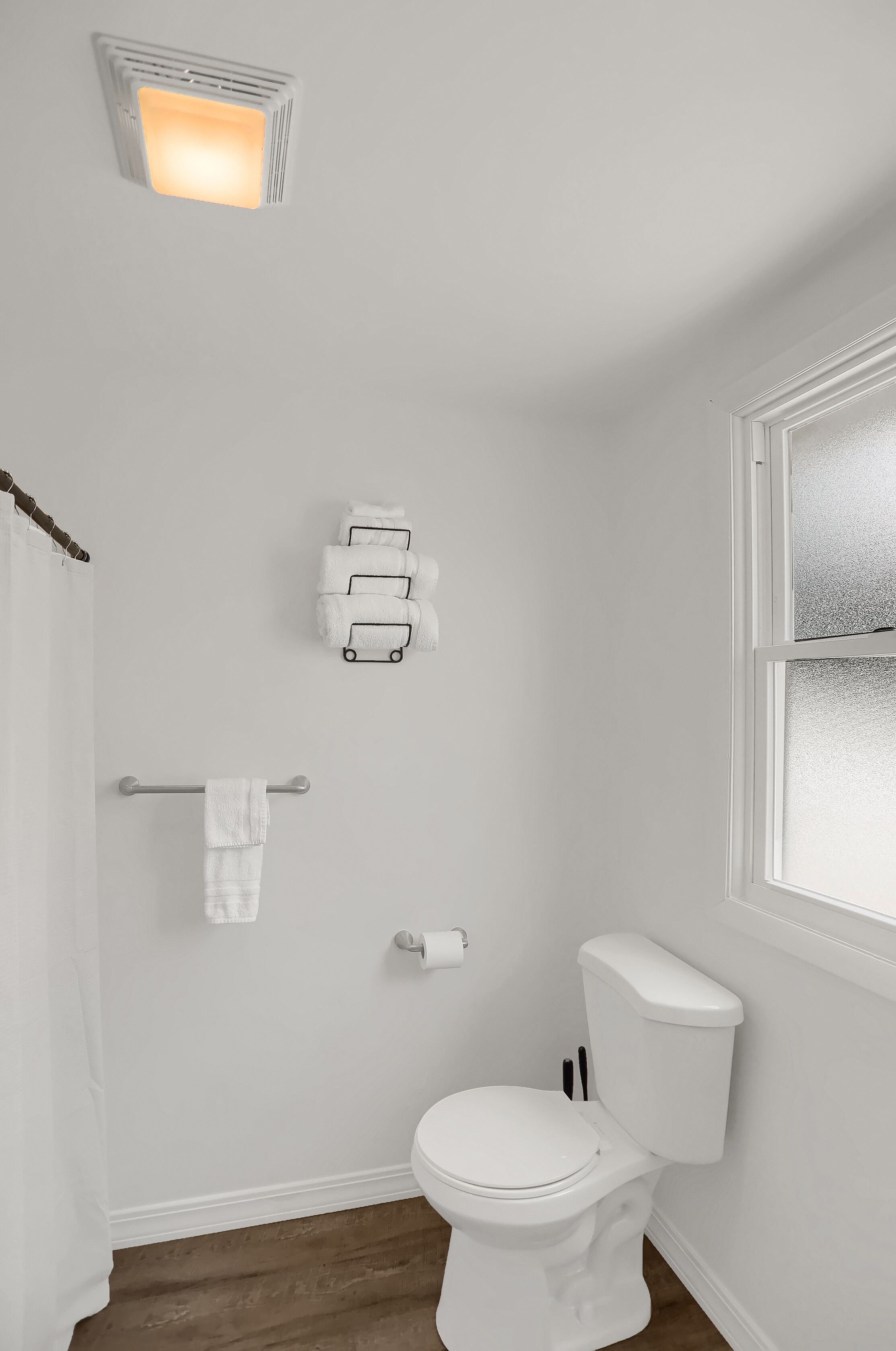 A bathroom with a white toilet, a towel rack, a towel dispenser, and a window with frosted glass.