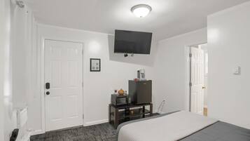 A hotel room with a bed, a TV mounted on the wall, a small table with a microwave and a refrigerator, and a door leading to another room.