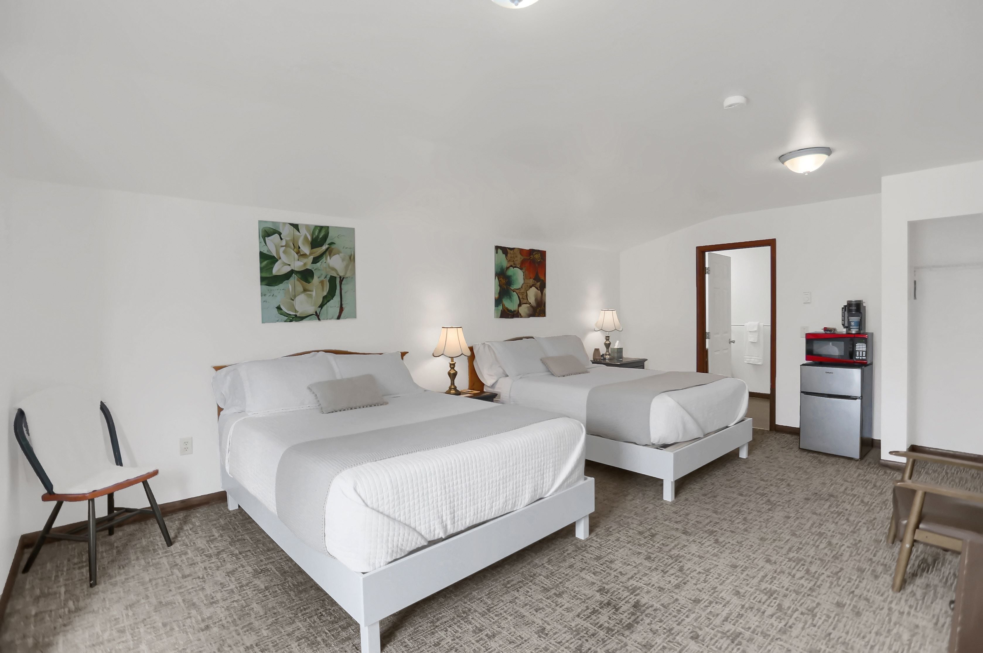 A hotel room with two beds, a desk, a chair, a microwave, and a refrigerator.