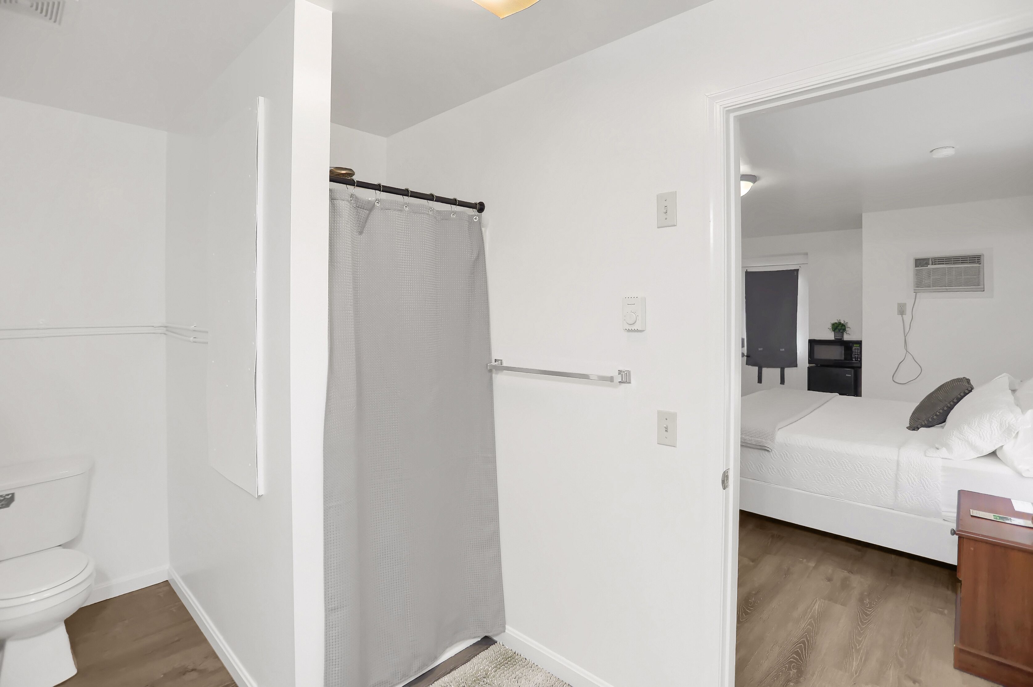 A bedroom with a bed, a bedside table, a nightstand, a window, and a door leading to another room.