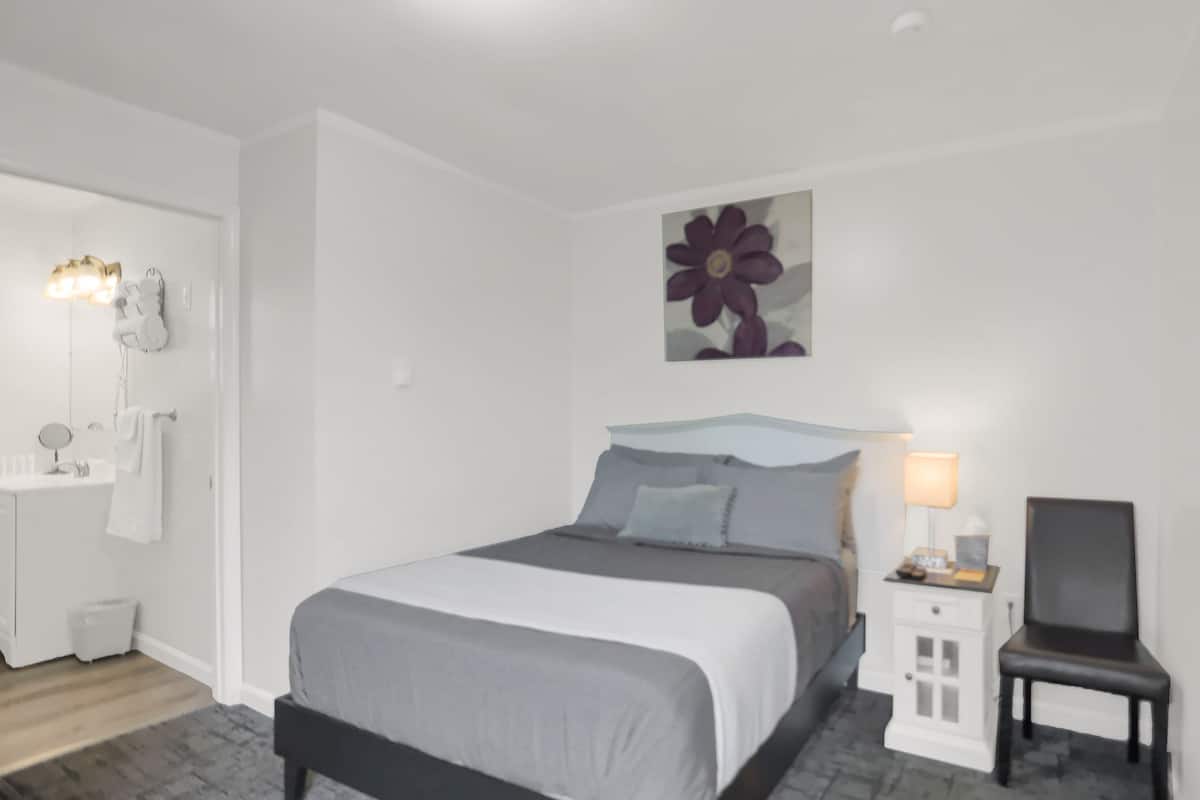 A bedroom with a bed, bedside table, chair, and a wall-mounted artwork.