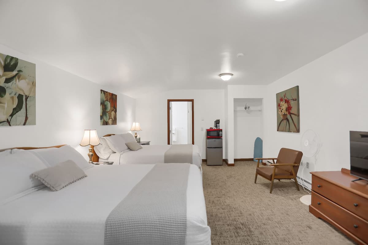 A hotel room with two beds, a desk, a chair, a TV, and artwork on the walls.