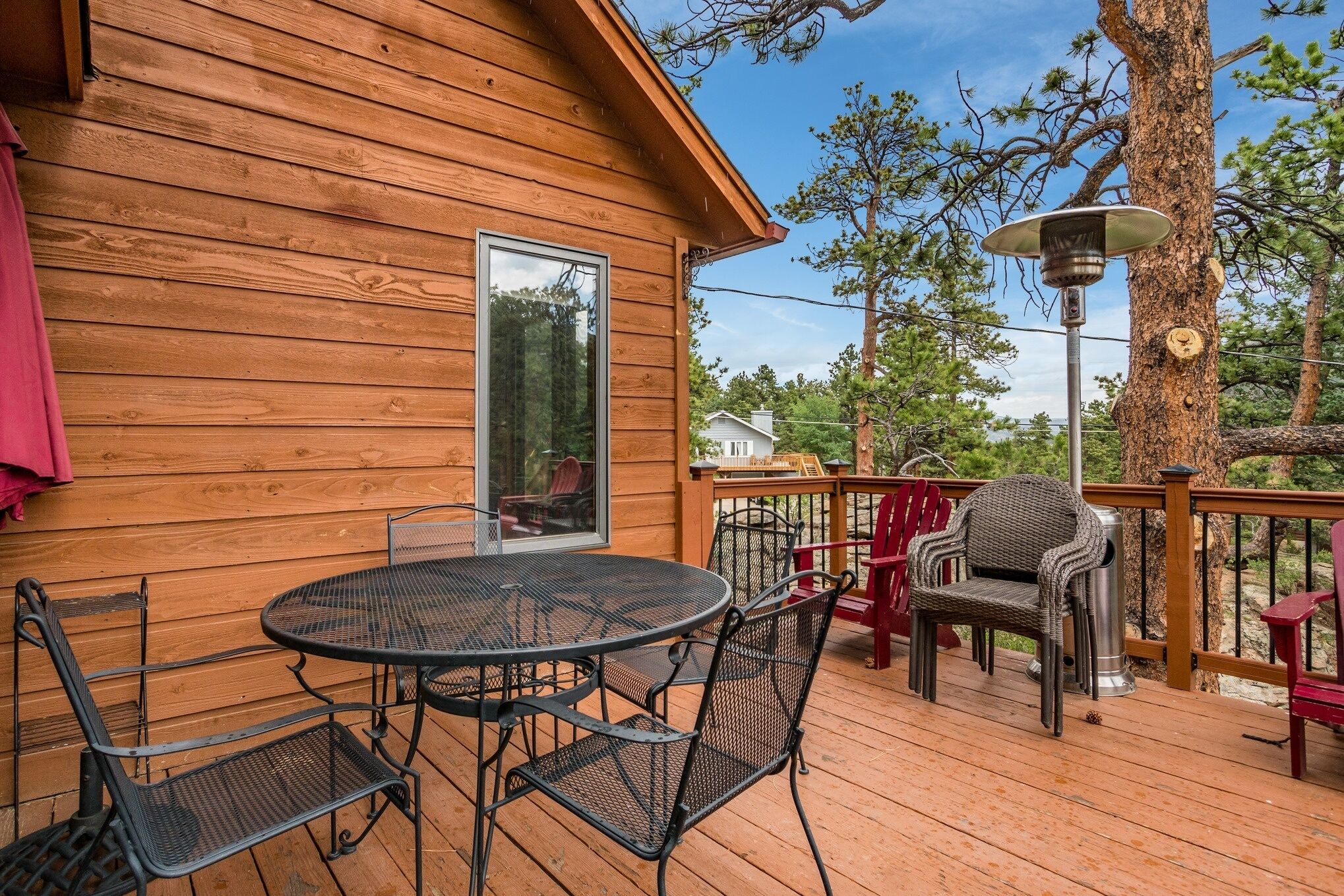 A wooden deck with a round table and chairs, a red bench, and a lamp post.