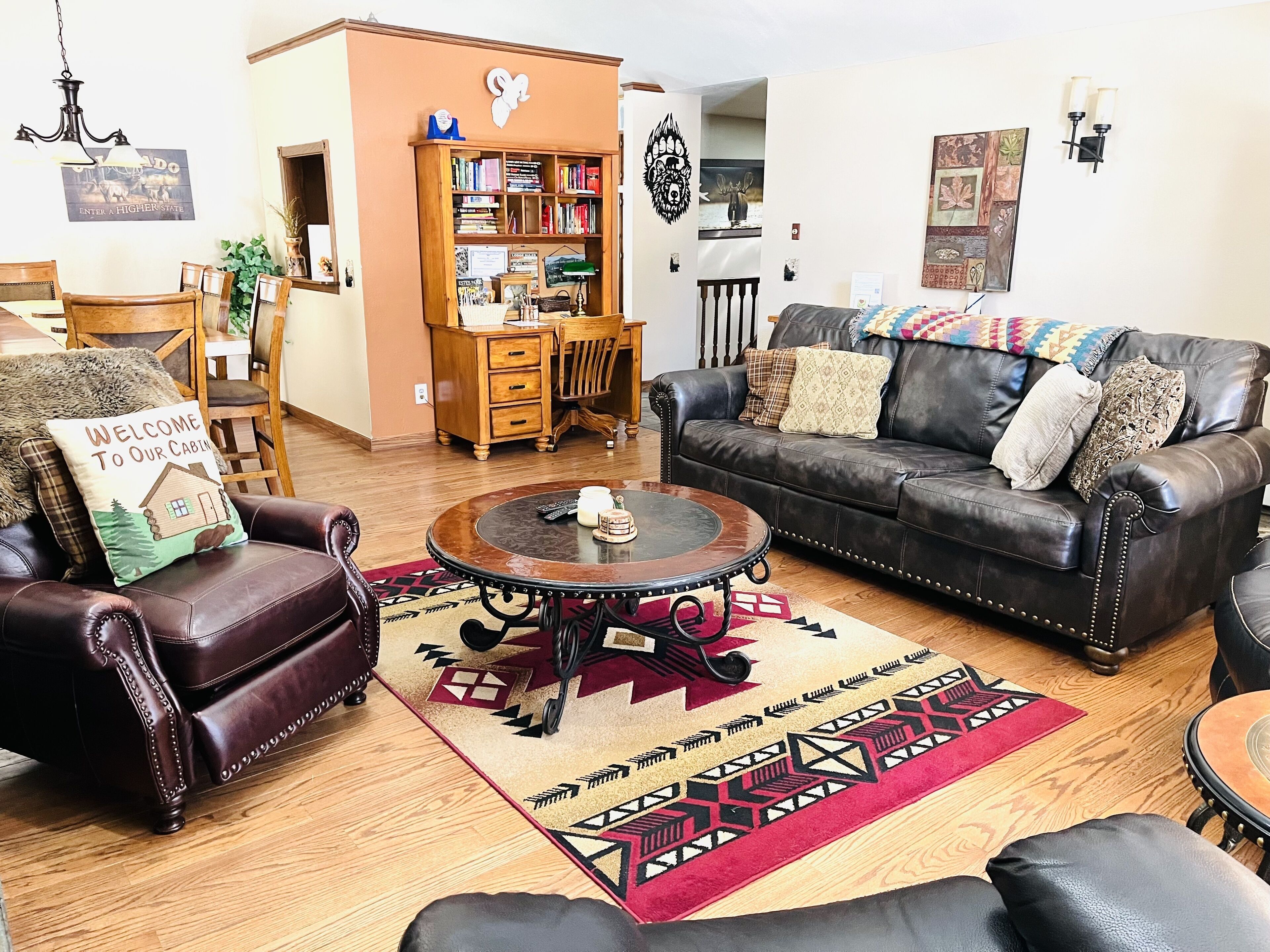 A living room with a leather sofa, a coffee table, a bookshelf, and a dining area with wooden furniture.