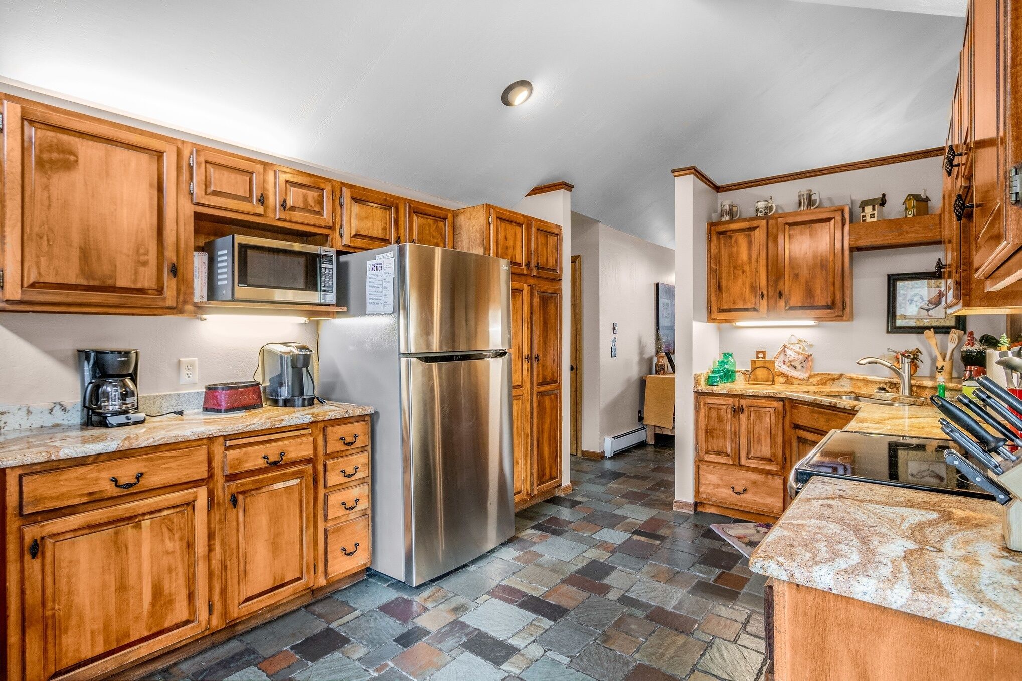 A kitchen with wooden cabinets, a stainless steel refrigerator, a microwave, and a granite countertop.