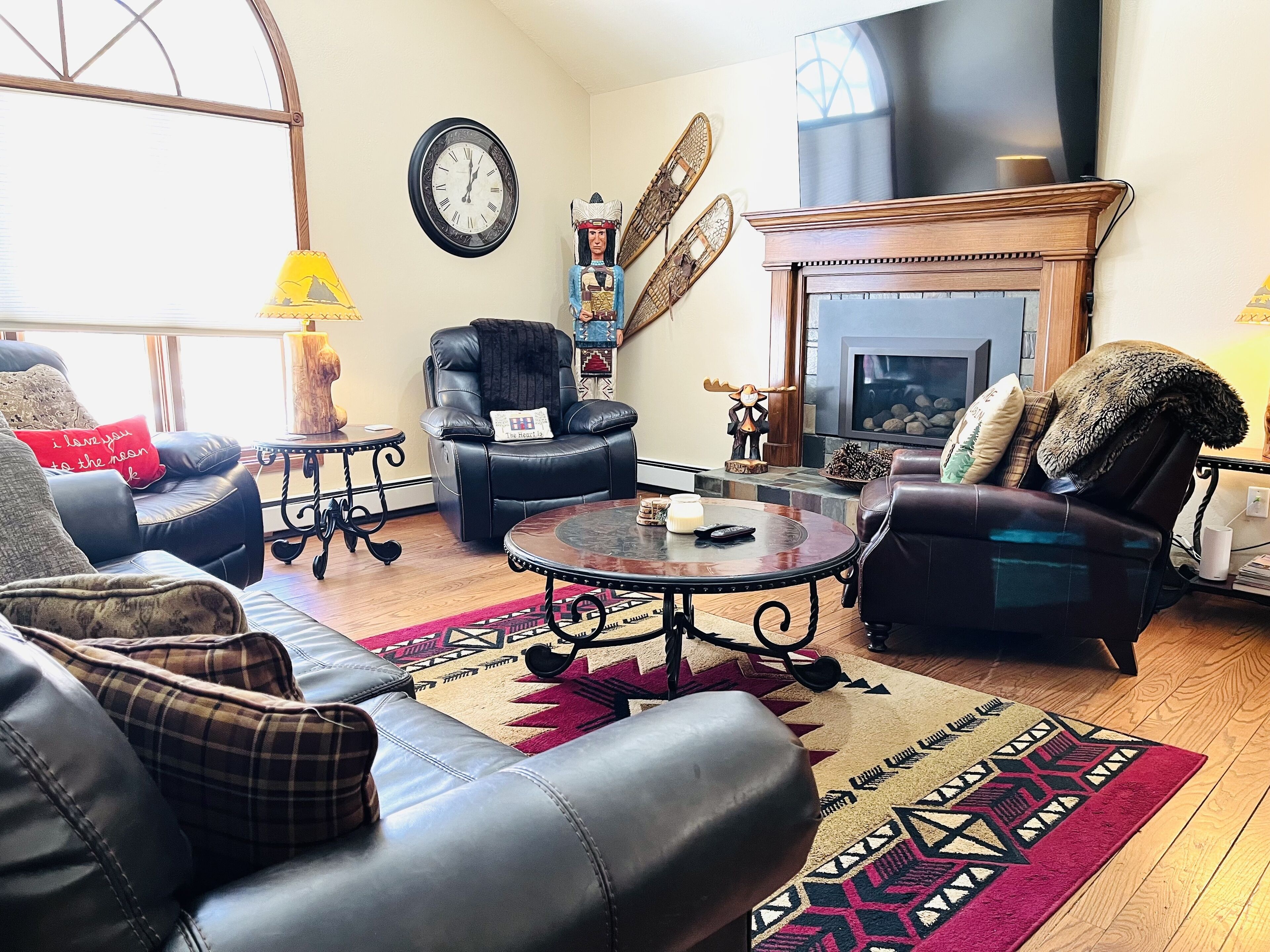 A cozy living room with leather sofas, a fireplace, a clock, and decorative wall art.