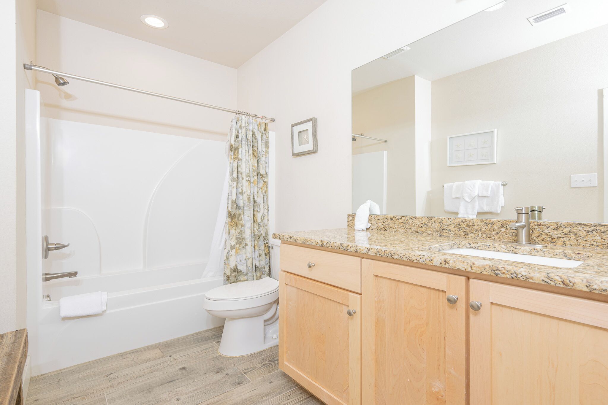 A bathroom with a bathtub, toilet, vanity with a sink, and a large mirror.