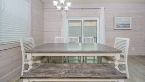 Un coin repas avec une table et des chaises en bois, un lustre et une vue sur l’extérieur par une porte.