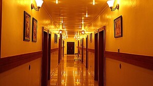 A hotel hallway with a polished floor, framed artwork on the walls, and wall-mounted light fixtures. - The Carlton Gate Hotel (Ibadan)