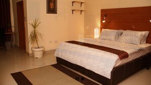 A bedroom with a bed, bedside table, lamp, and a potted plant. - The Carlton Gate Hotel (Ibadan)