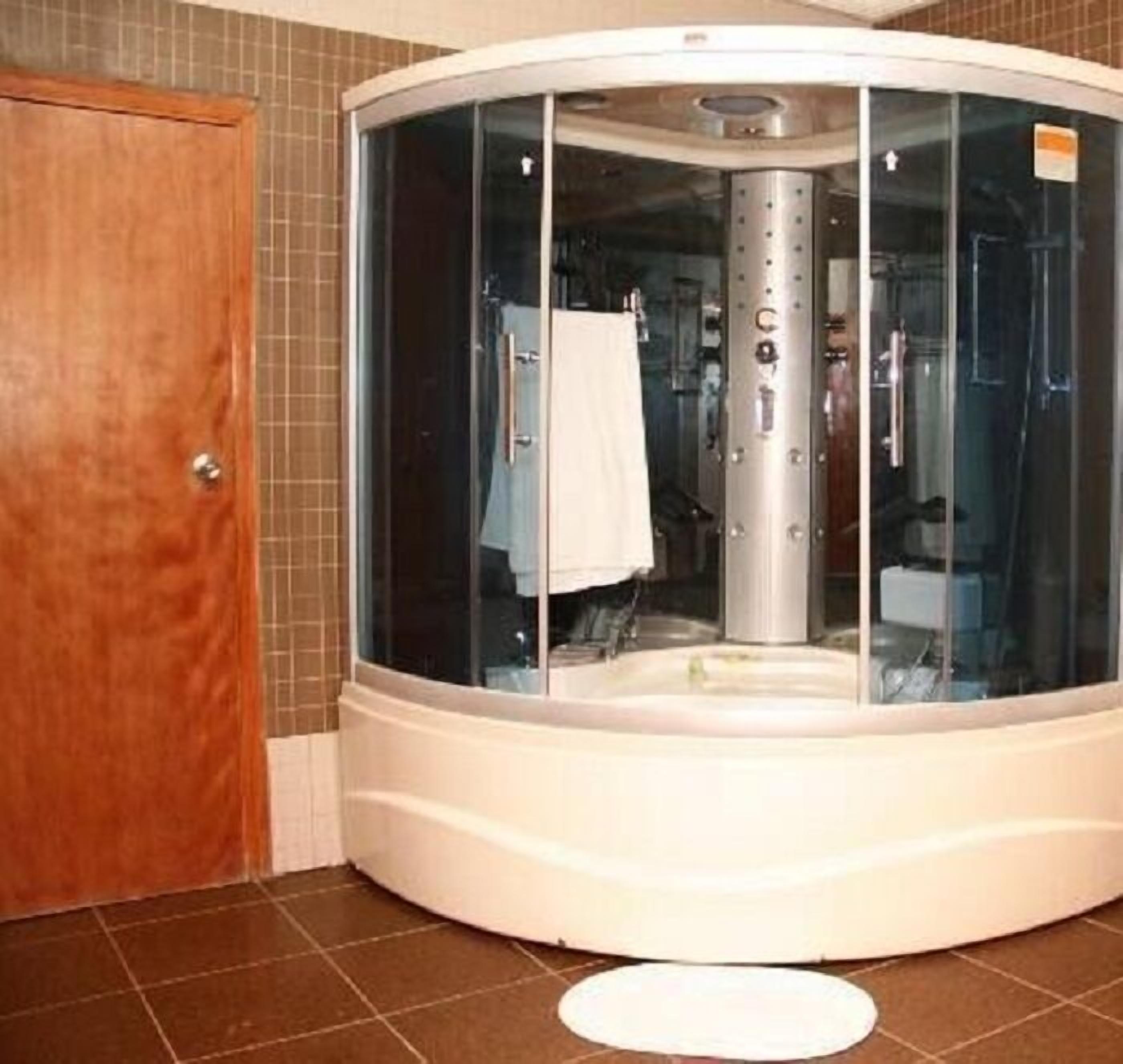A modern bathroom with a glass-enclosed steam room, a wooden door, and tiled flooring.