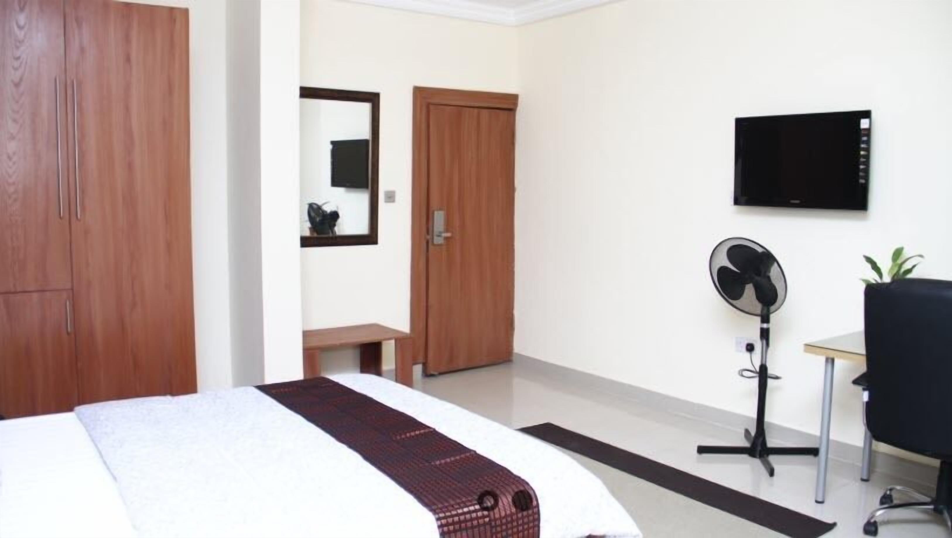 Una habitación de hotel con cama, escritorio, silla, televisor, espejo y armario.