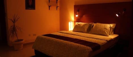 Une chambre à coucher avec un lit, une table de chevet, une lampe fixée au mur et une plante en pot.