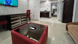Uma sala de estar moderna com uma TV de tela plana, uma mesa de centro de vidro, uma cadeira vermelha e um sofá marrom.