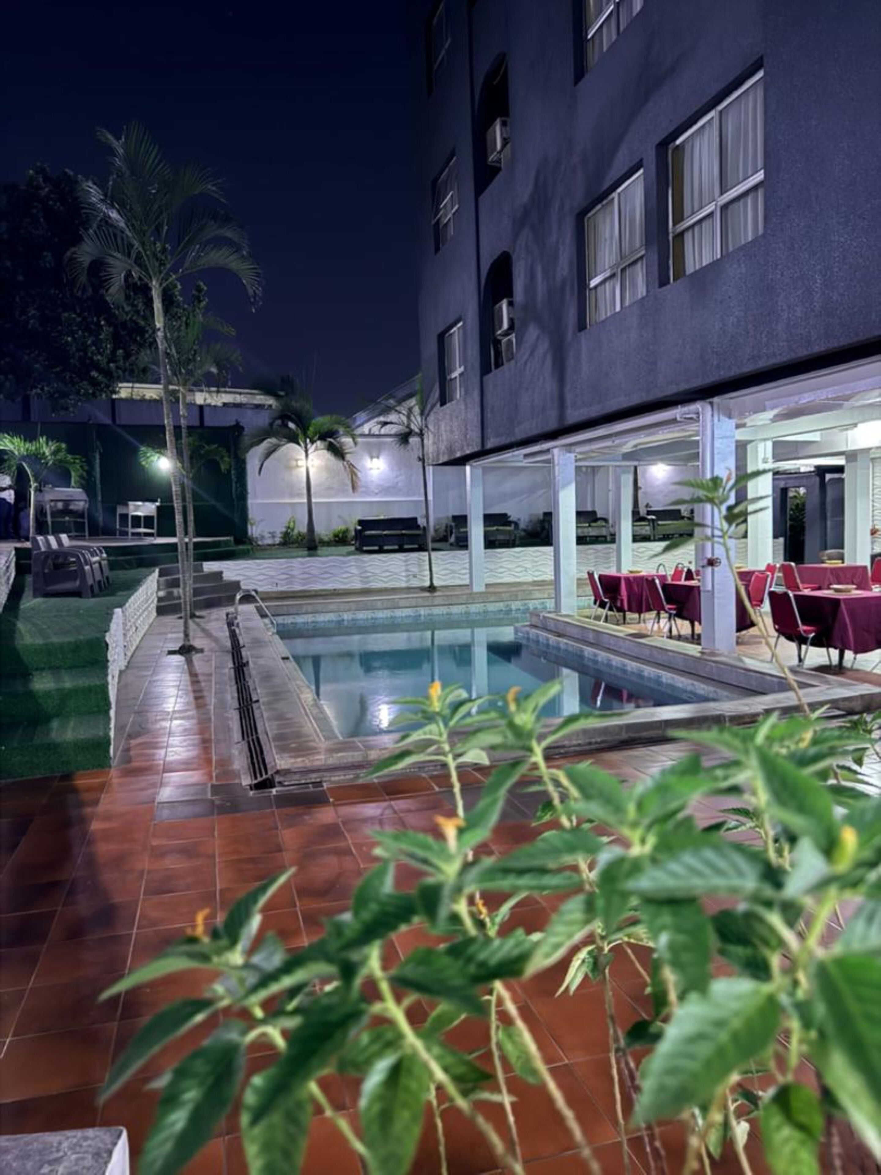 A pool area with a covered seating area and a building in the background.