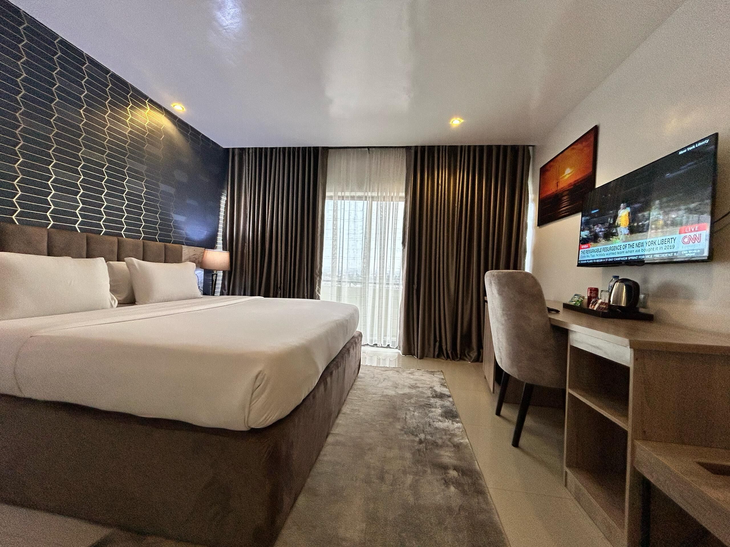 Une chambre d’hôtel moderne, dotée d’un grand lit, d’un bureau et d’un téléviseur fixé au mur.
