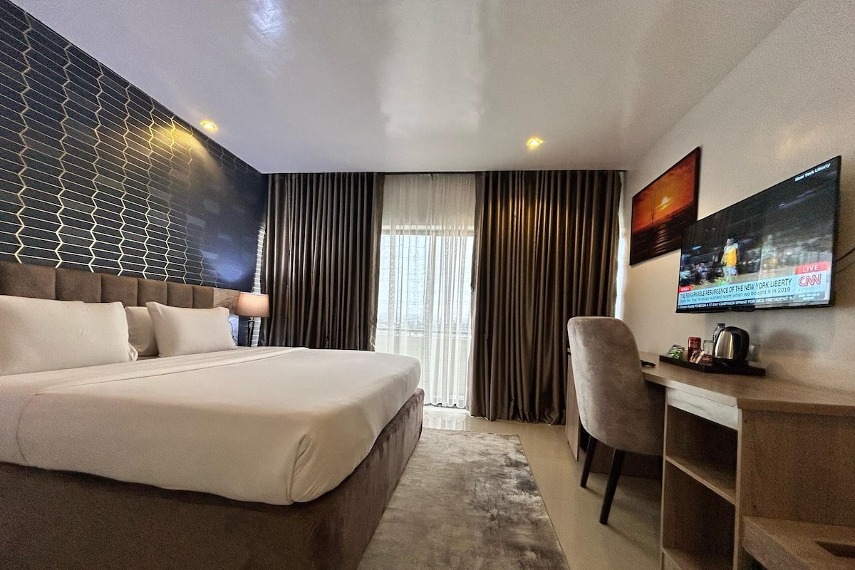 A modern hotel room with a large bed, a desk, and a TV mounted on the wall.