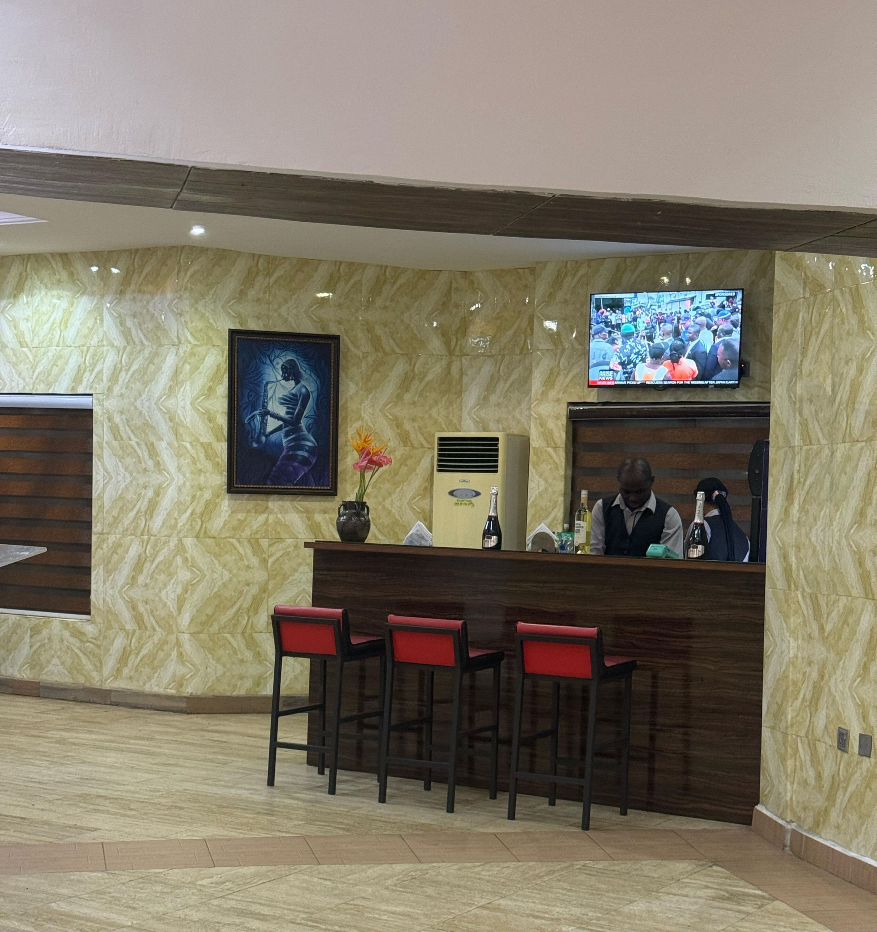 A reception area with a marble wall, a framed artwork, a television, and a bar with red chairs.