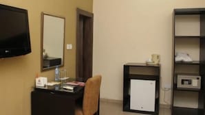 A hotel room with a flat-screen TV, a desk with a chair, a mirror, a small refrigerator, and a shelf with a microwave. - Class Suites Signature (Lagos)