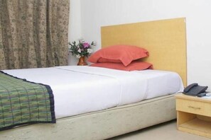 A hotel room with a bed, a nightstand, a telephone, and a vase with flowers. - Eagles Park 1960 (Lagos)