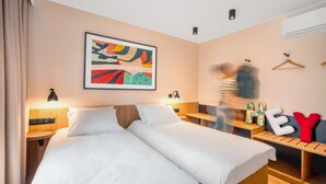 A hotel room with two beds, a bedside table, a wall-mounted air conditioner, and a colorful abstract painting. - Suntago Village (Mszczonow)