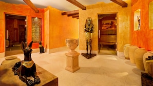 A room with a statue of a figure in a golden outfit, a black dog statue, and a large vase on a pedestal. - Suntago Village (Mszczonow)