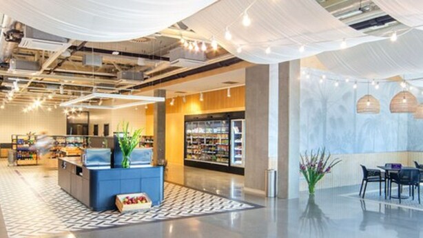 A modern interior with a reception desk, seating area, and a section with shelves. - Suntago Village (Mszczonow)